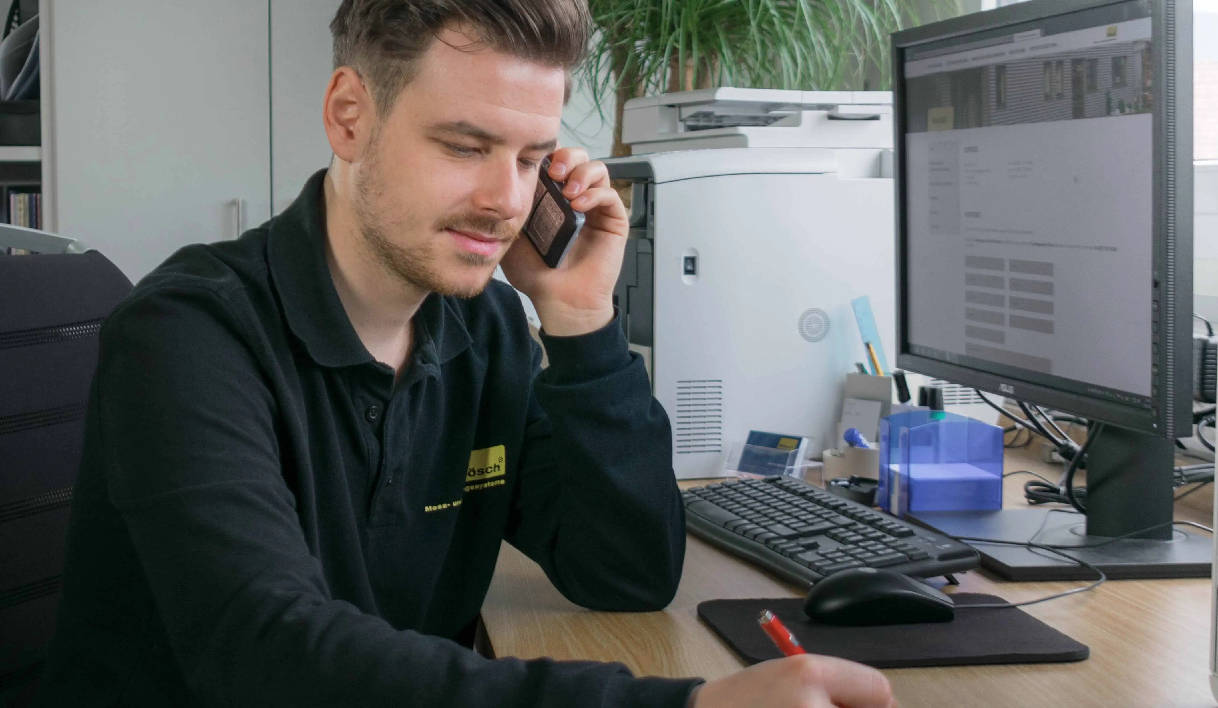 Mann, der am Schreibtisch am telefonieren ist und im Hintergrund der Computer